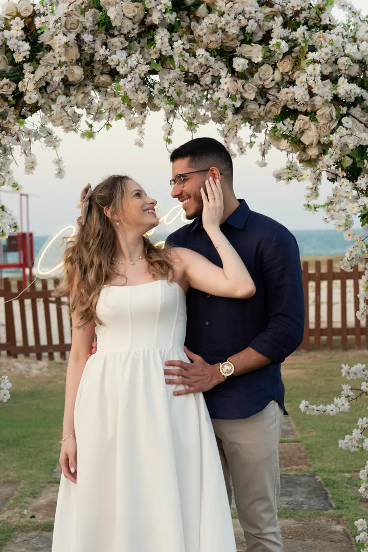 Juliana toca o rosto de Davi enquanto os dois se olham sob o arco de flores